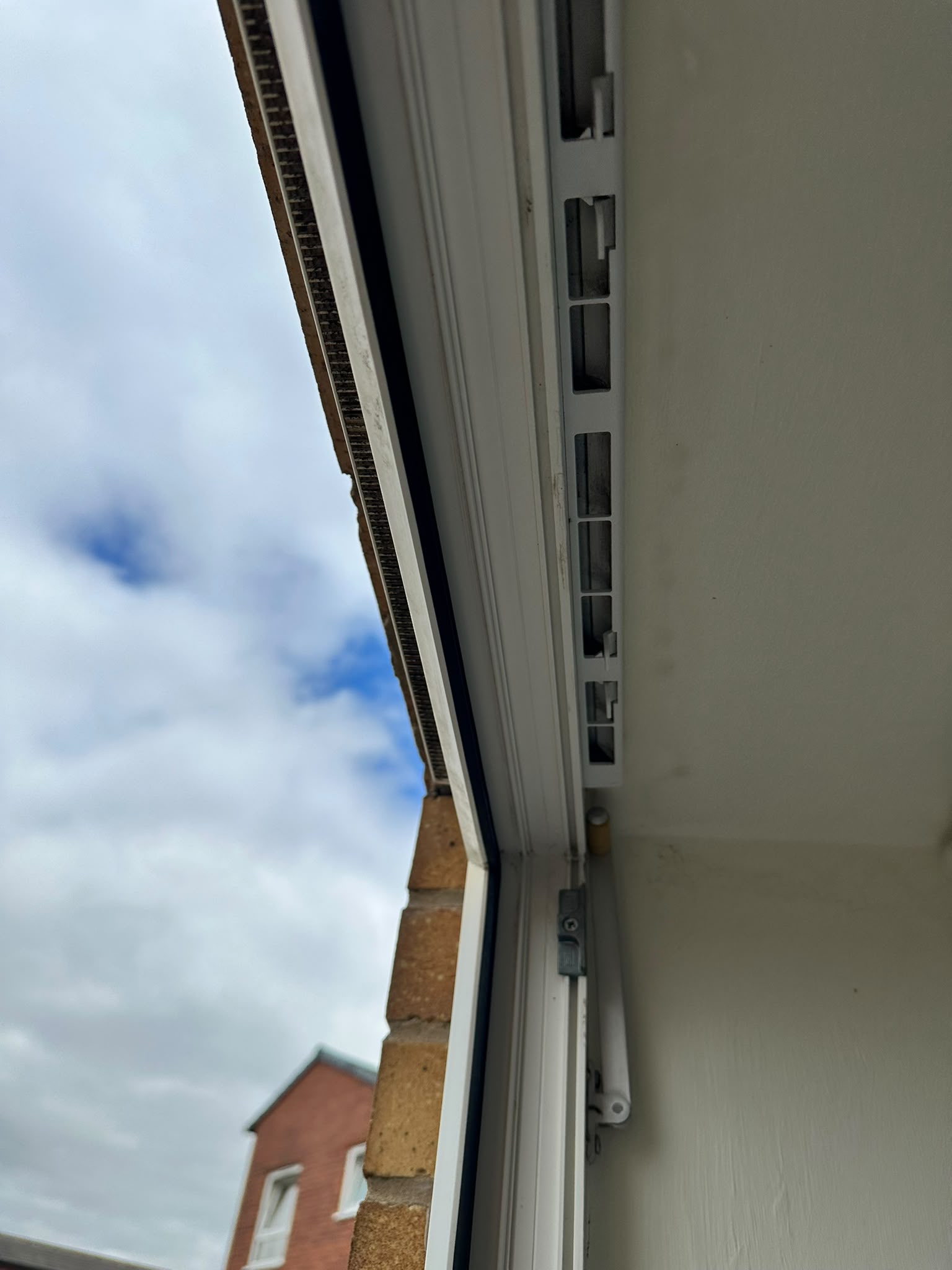 Open white uPVC window with a trickle vent, looking out at a neighbouring brick house